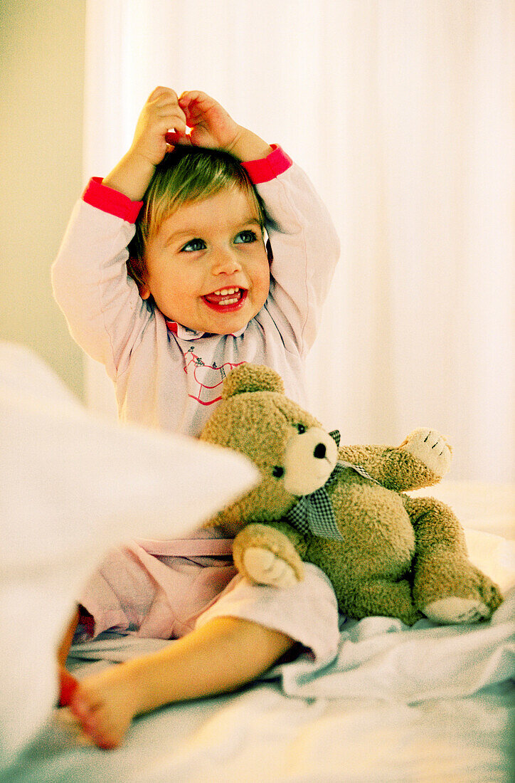 Toddler girl sitting with teddy sitting on bed, portrait