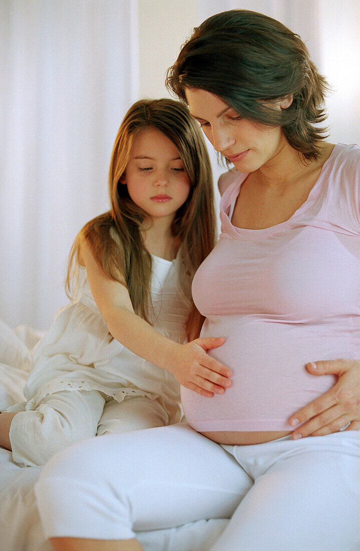 Mädchen berührt den Bauch ihrer schwangeren Mutter