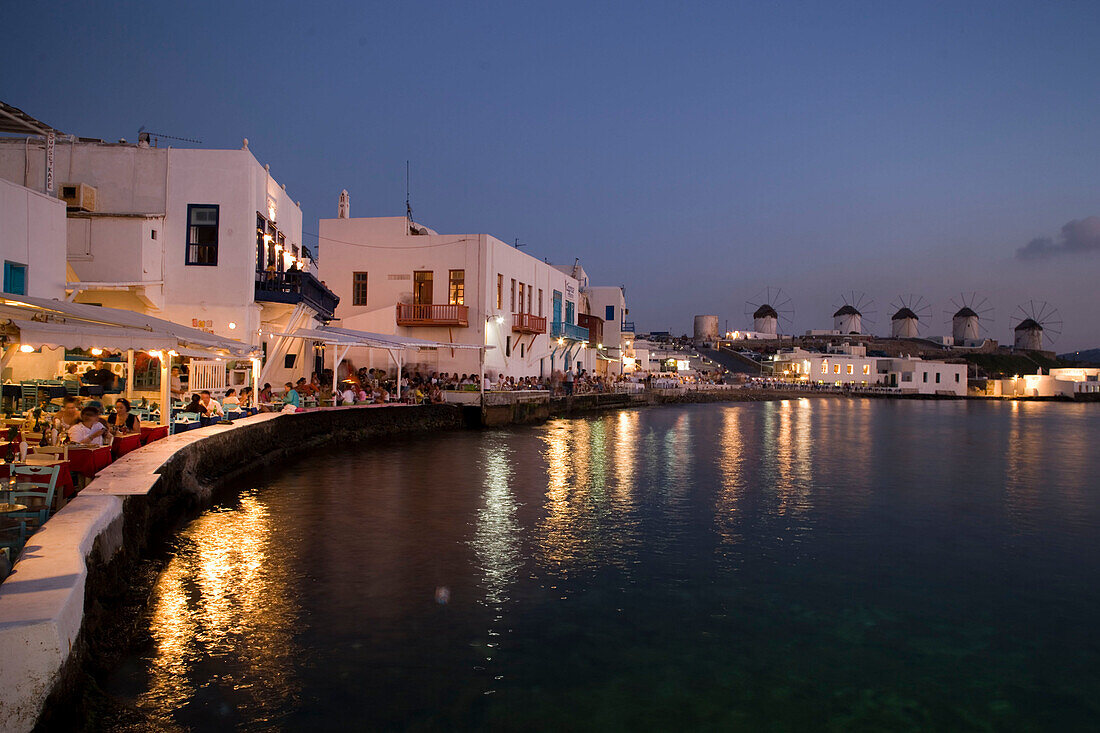 View along bank with restaurants and bars in the evening, windmilles in background, Little Venice, Mykonos-Town, Mykonos, Greece