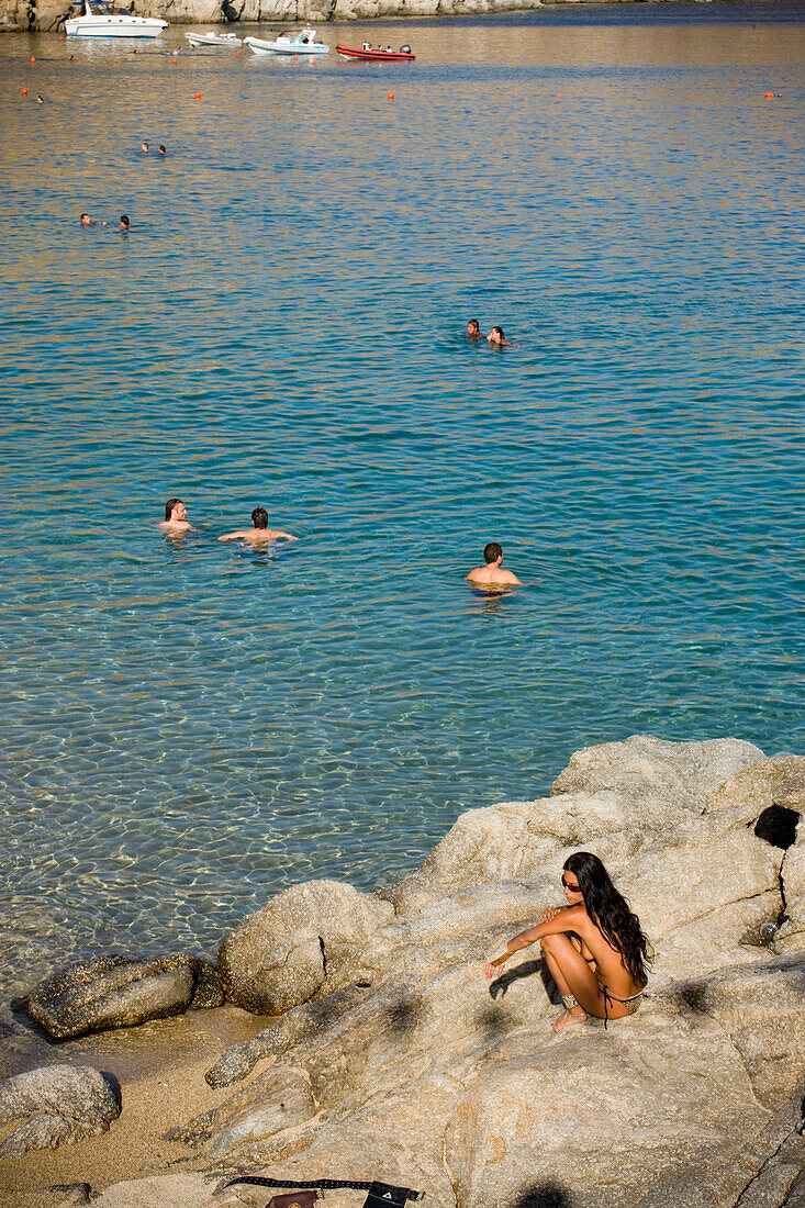 View from a woman sitting on a rock to bathing people at Super Paradise Beach, knowing as a centrum of gays and nudism, Psarou, Mykonos, Greece