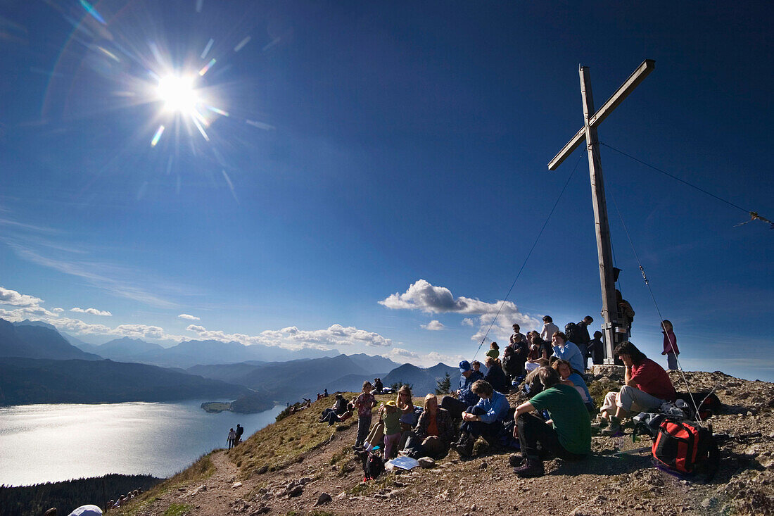 Large group of hikers looking from Jochberg summit onto Lake Walchensee, Upper Bavaria, Germany