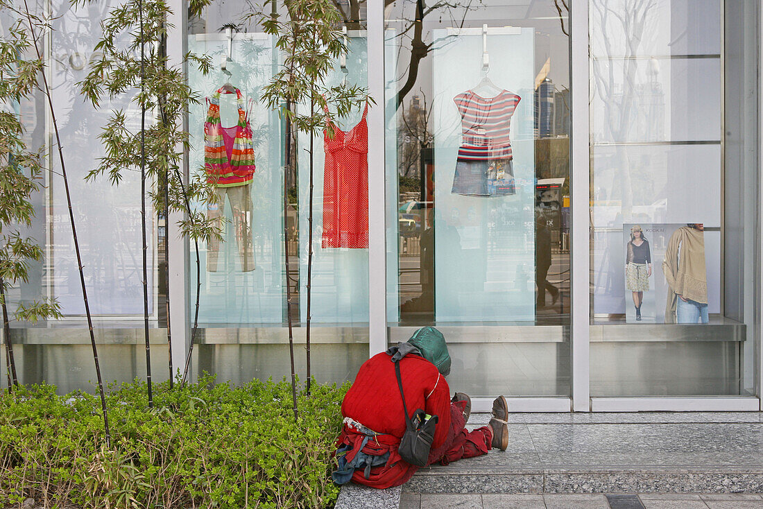 Homeless sits in front of fashion shop window
