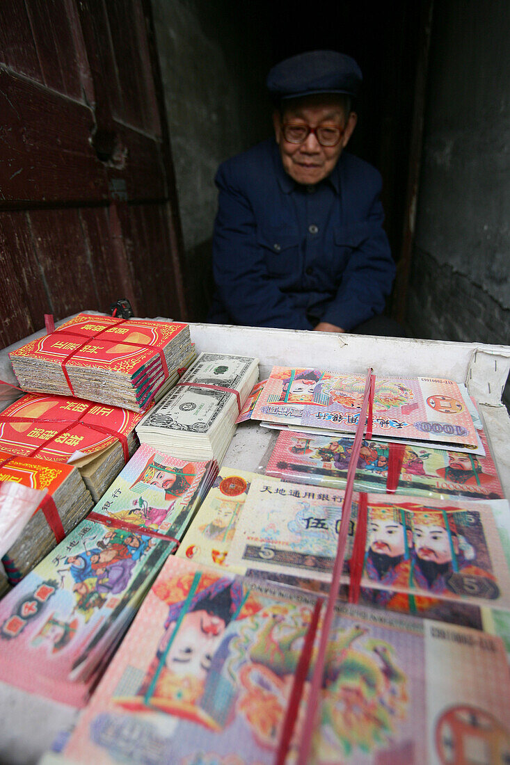 Old man at stall with bundles of ghost money, Paper money offerings, spirit money