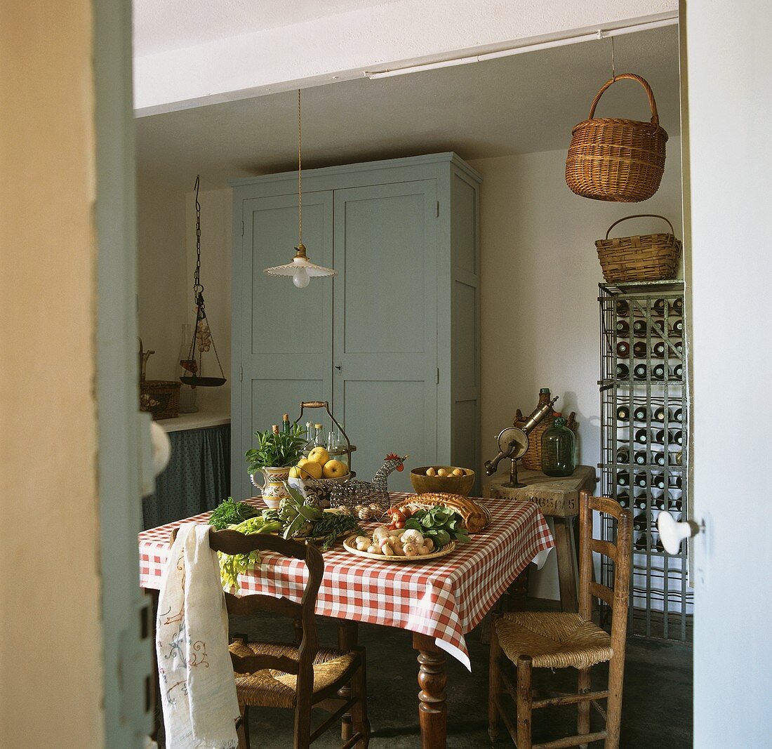 Vegetables and herbs on a dining table with a wine rack in the background