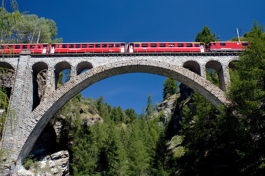 Zug fährt über Viadukt unter blauem Himmel, Guarda, Graubünden, Schweiz