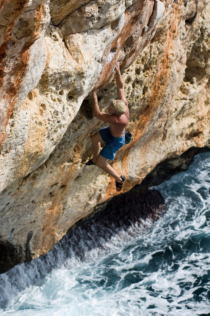 Man climbing on rock face over water, Coast of Majorca, Spain