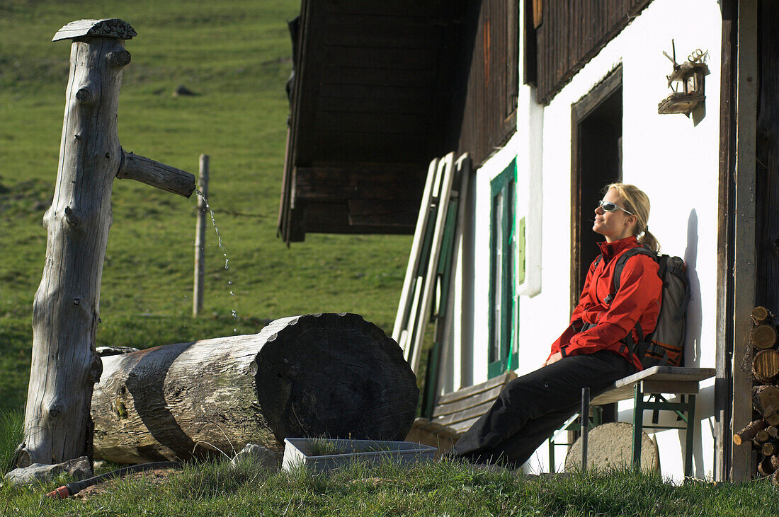 Young female hiker relaxing in front of wooden cabin on alp, Salzburger Land, Austria