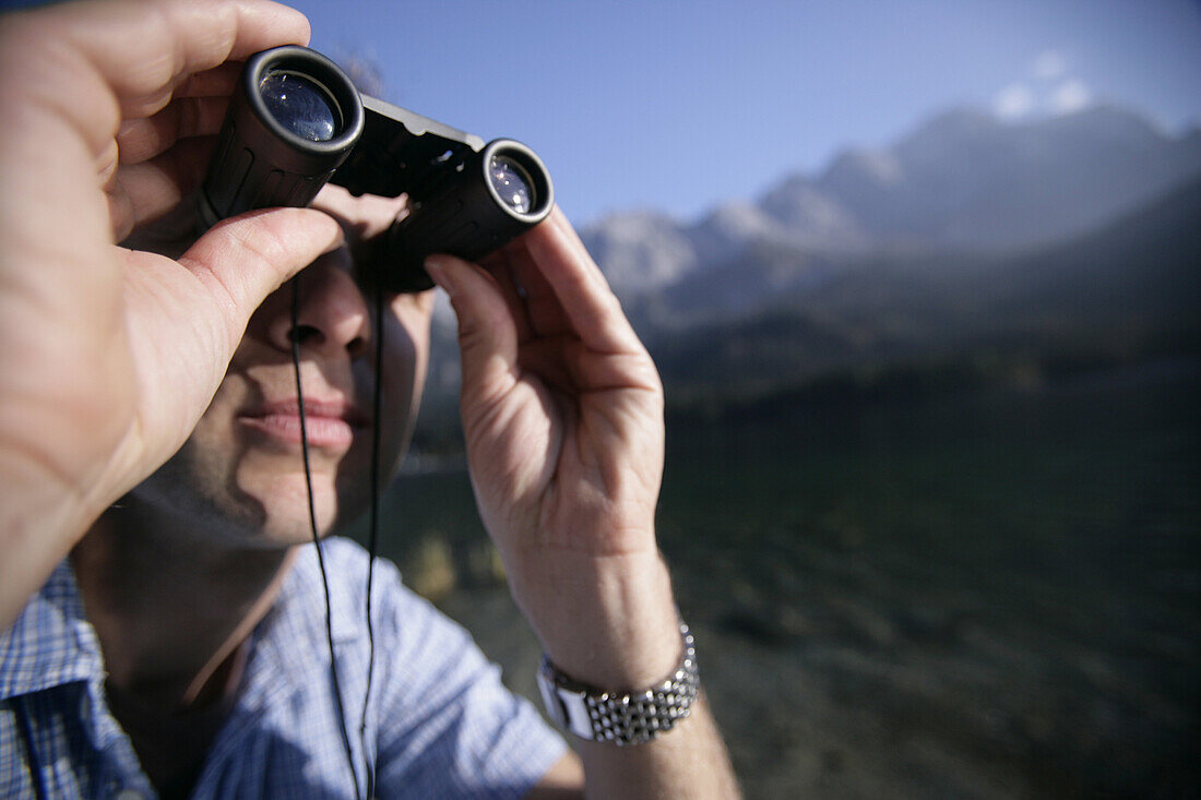Man on shore of alpine lake with binocular ,lake eibsee, Zugspitze in back, Bavaria, Germany