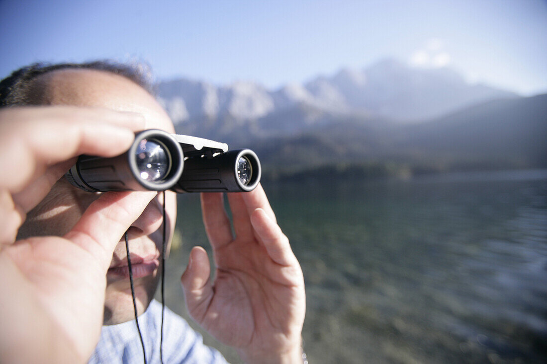 Man on shore of alpine lake with binoculars,lake eibsee, Zugspitze in back, Bavaria, Germany