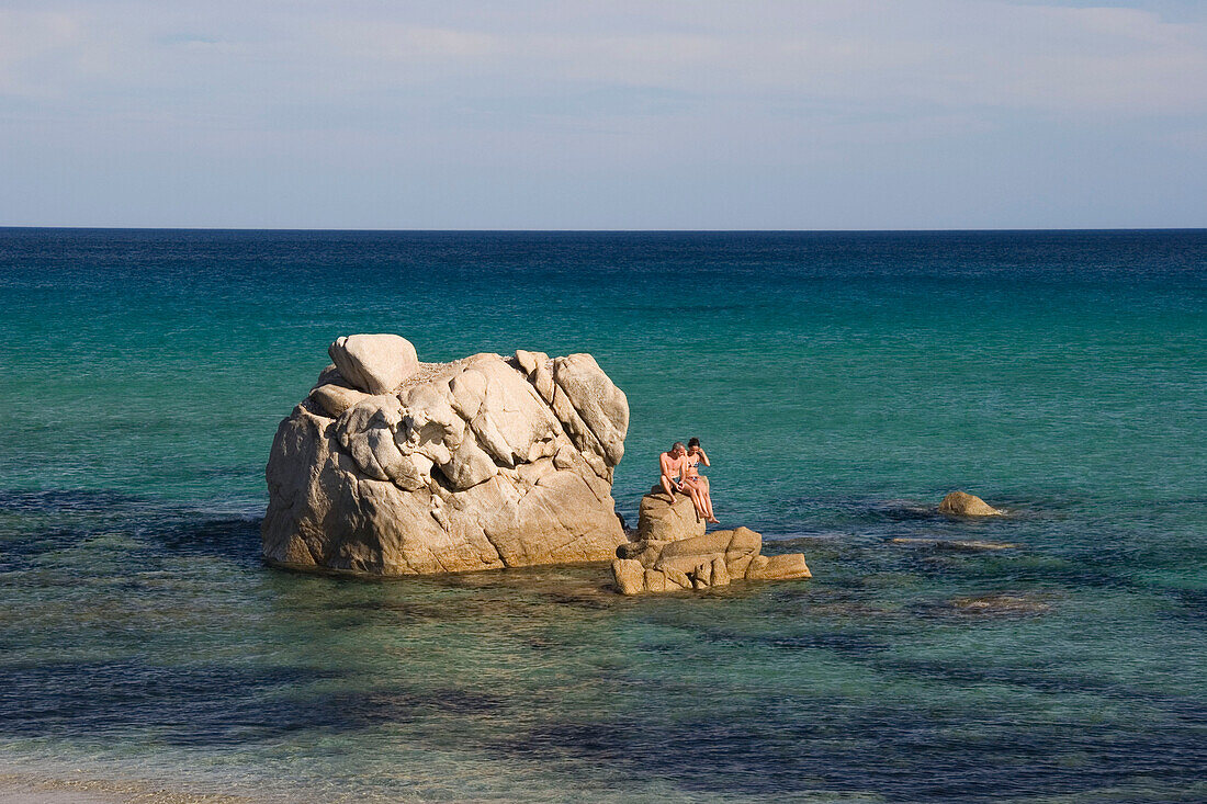 Couple sitting on rock, Costa Rei, Sardinia, Italy