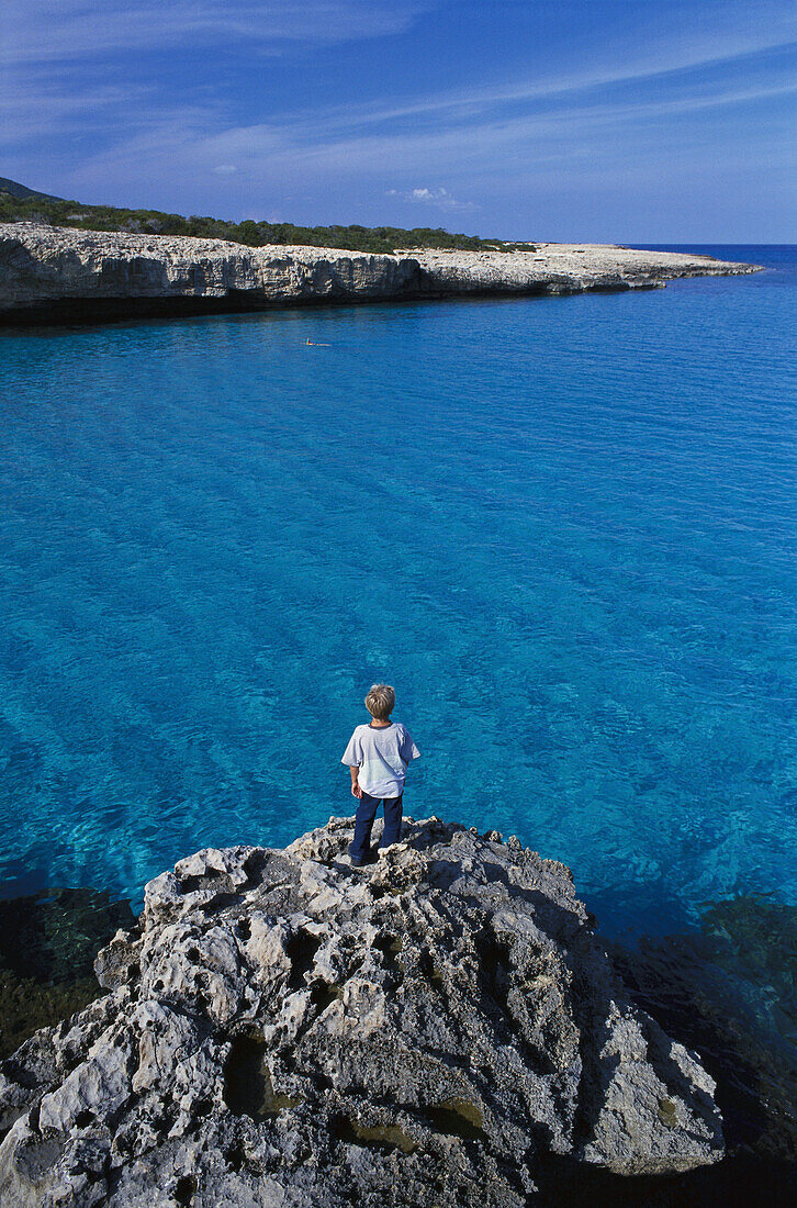 Boy standing on rock, coast near Fontana Amorosa, Akamas peninsula, Cyprus