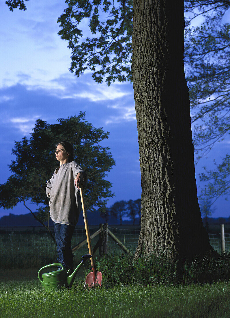 Woman with spade and watering can, standing in garden