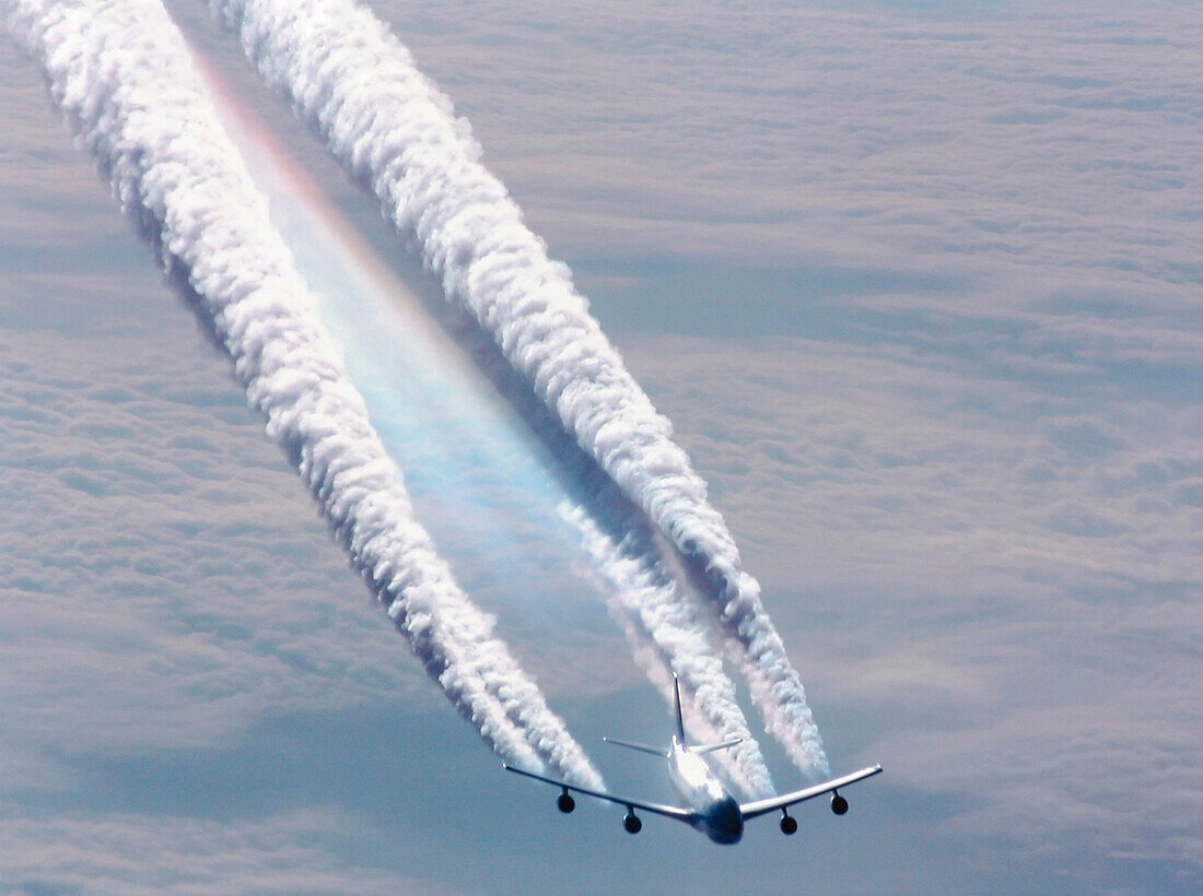 Plane flying over sea of clouds leaving huge condensation trails