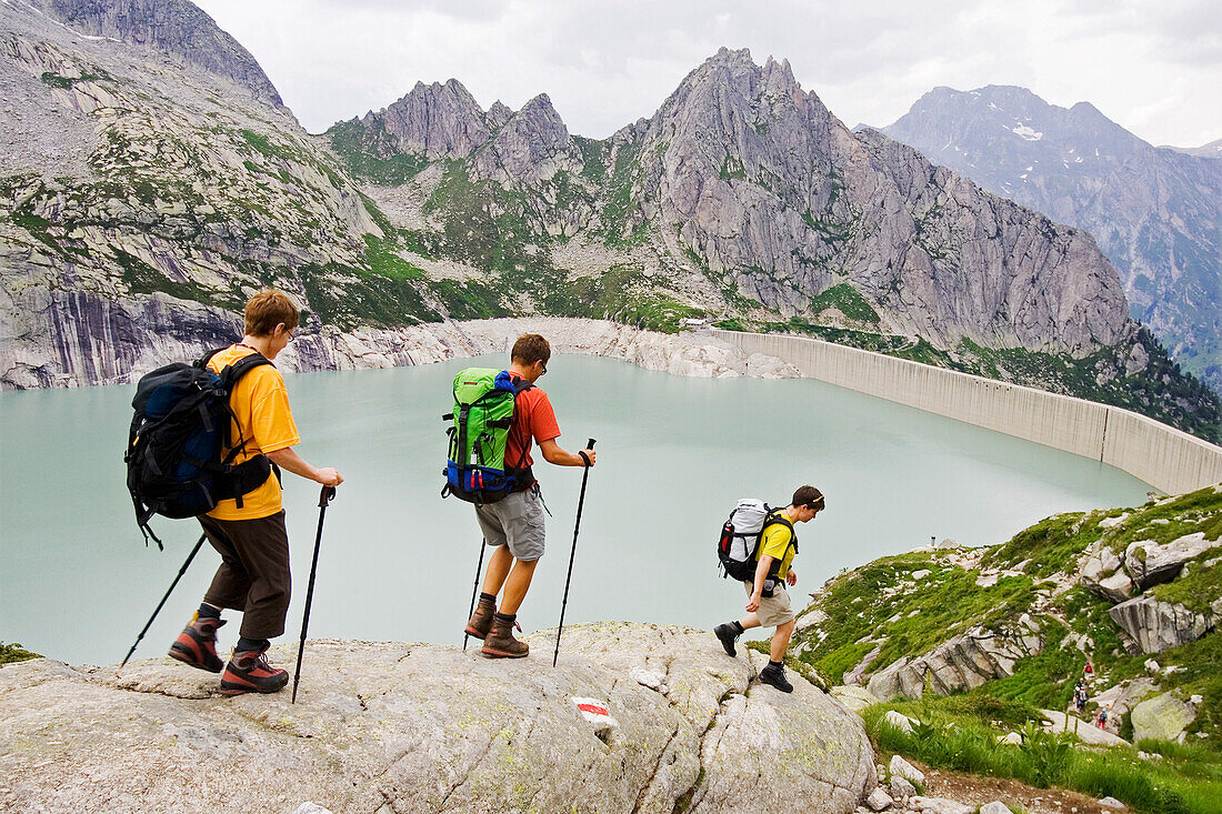Three hikers scrambling down over a rocky path towards the albigna lake, Albigna Lake, Bergell, Bregaglia, Graubuenden, Grisons, Switzerland