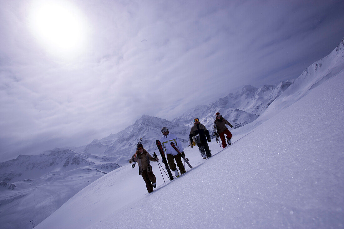 Four people with skies and snowboard walking up a snowcapped mountain, Kuehtai, Tyrol, Austria