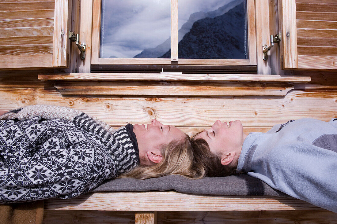 Two young women sunbathing, lying on bench of ski lodge, Kuehtai, Tyrol, Austria