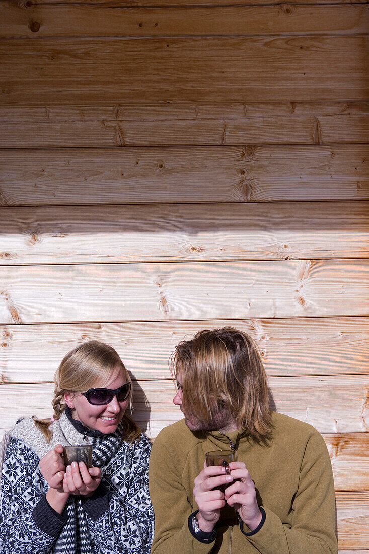 Couple sunbathing on terrace of ski lodge, drinking tea, Kuehtai, Tyrol, Austria