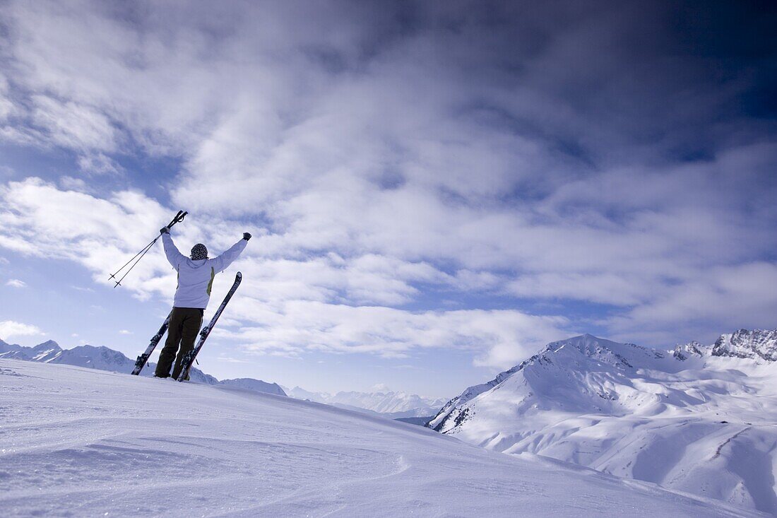 Young man with skis standing on snowcovered mountain, arms rising high, Kuehtai, Tyrol, Austria