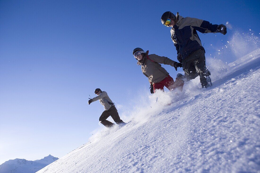 Gruppe junger Menschen laufen im Schnee den Berg hinunter, Kühtai, Tirol, Österreich