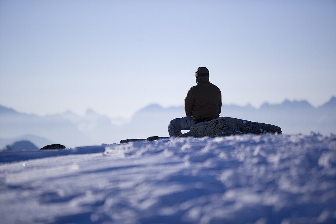 Mann sitzt neben der Skipiste und genießt die Aussicht, Kühtai, Tirol, Österreich