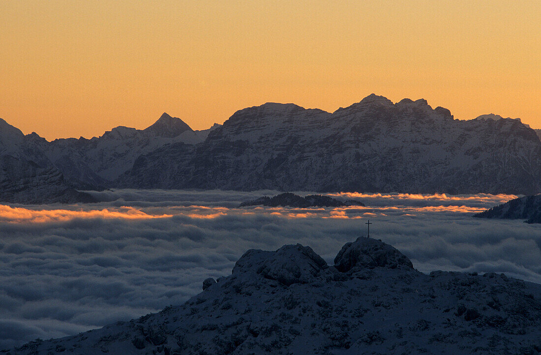 Cross on a summit with fogbank at dawn, view from Wendelstein towards Loferer Steinberge, Bavarian range, Upper Bavaria, Germany