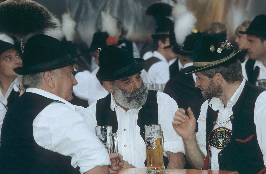 Three men in traditional dress talking, one wearing a hat with tufts of chamois hair, maypole festival, Flintsbach, Upper Bavaria, Germany