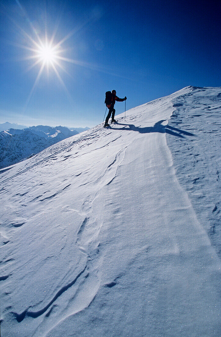 Ein Mann steigt mit Skiern zu einem verschneiten Berggipfel auf. Parsenn, Davos, Graubünden, Bündnerland, Schweiz, Alpen, Europa, MR.