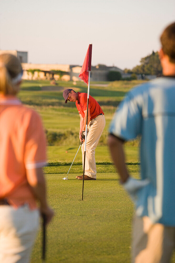 Male golfer preparing to hit ball, woman and man looking to him, Apulia, Italy