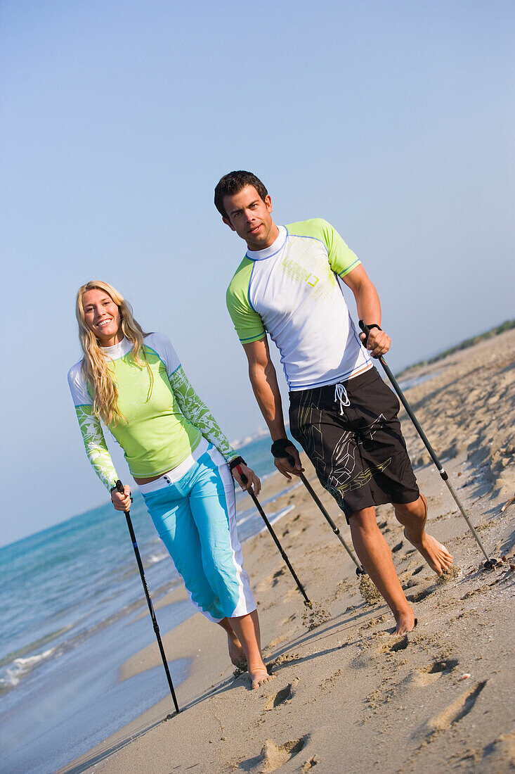 Couple walking with poles on beach, Apulia, Italy