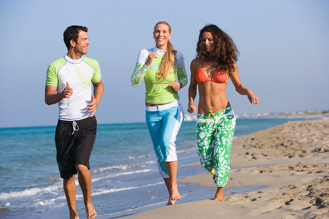 Drei junge Leute joggen am Strand, Apulien, Italien