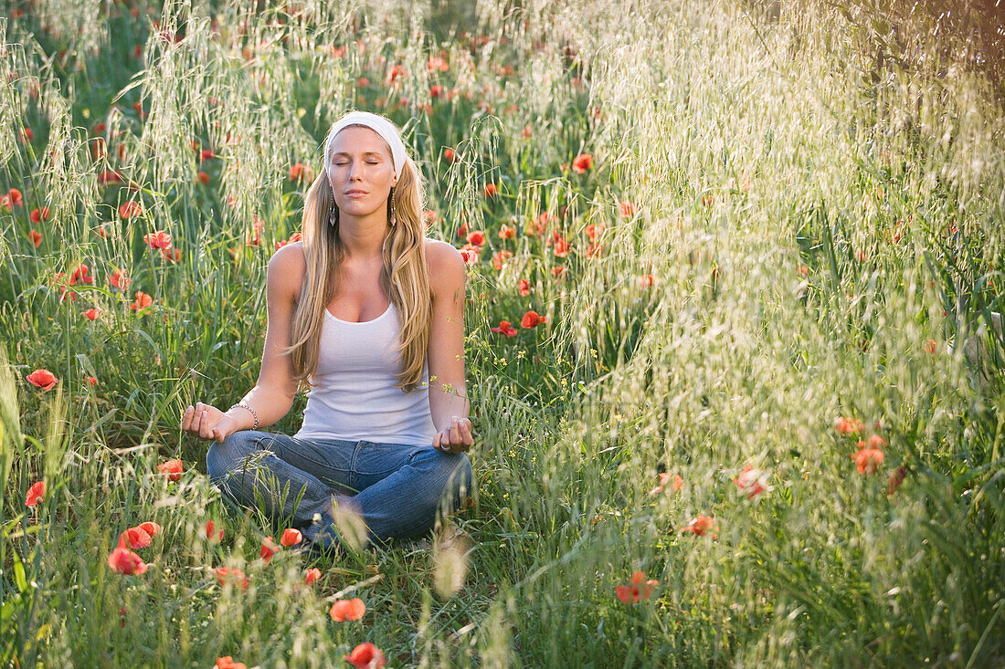 Junge Frau meditiert in Blumenwiese, Apulien, Italien