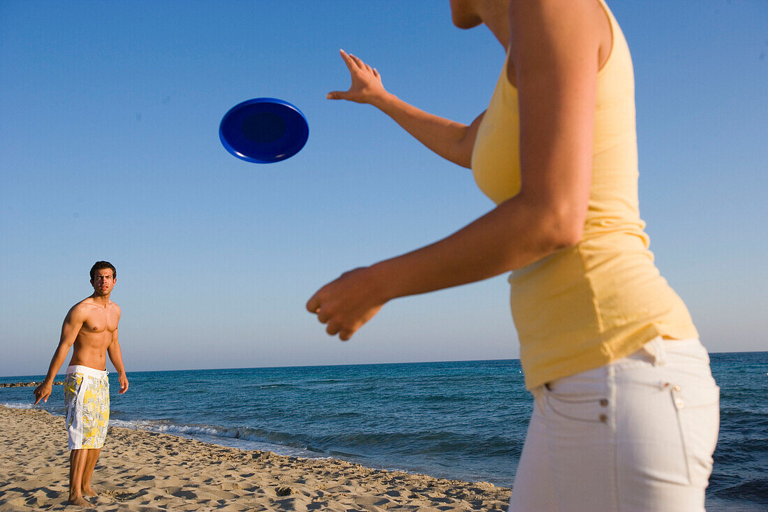Junges Paar spielt Frisbee am Strand, Apulien, Italien