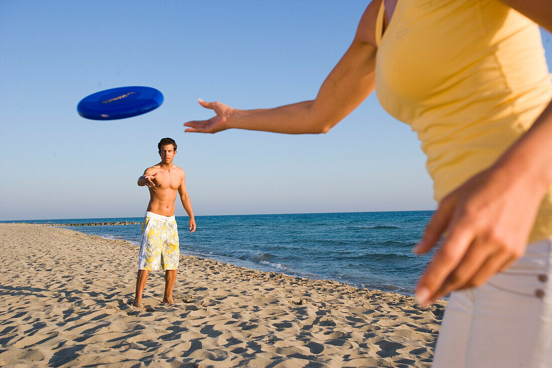 Junges Paar spielt Frisbee am Strand, Apulien, Italien