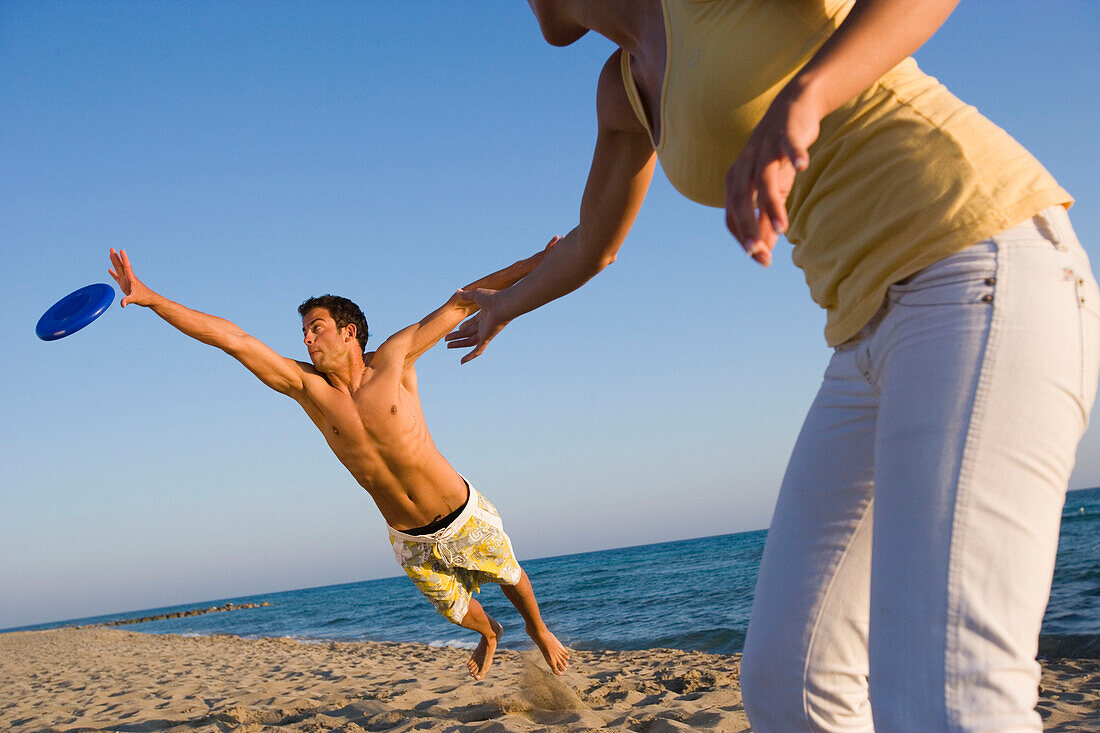 Junges Paar spielt Frisbee am Strand, Apulien, Italien