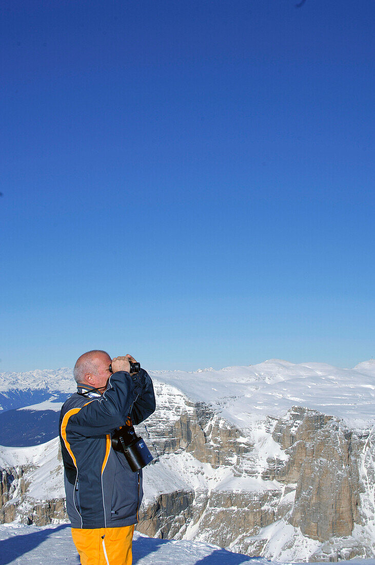Man with binoculars in front of snow covered mountains, Passo Pordoi, Dolomites, Italy, Europe