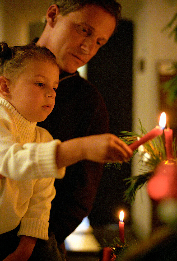 Girl (3-4 years) light up a candle on christmas tree