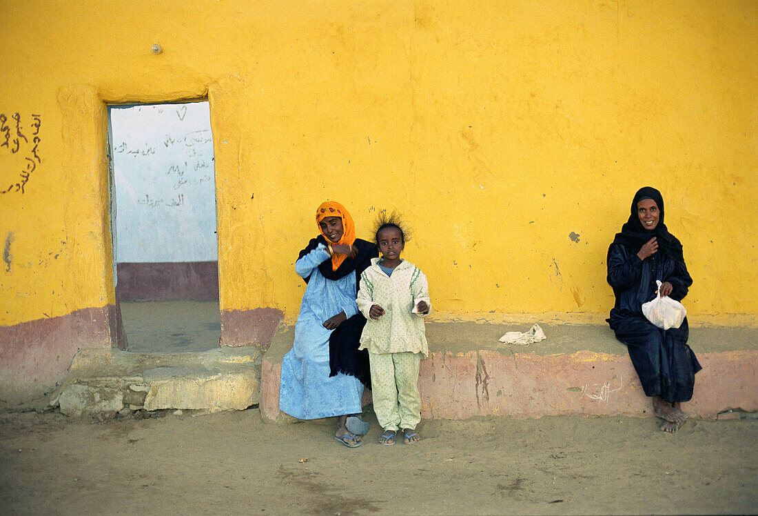 Egyptian people sitting in front of a yellow wall, Aswan, Egypt