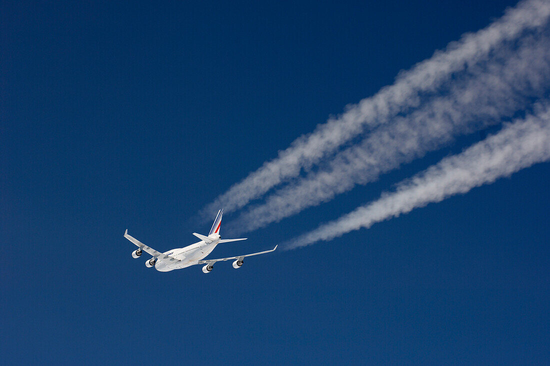 Flugzeug mit Kondensstreifen vor dunkelblauem Himmel