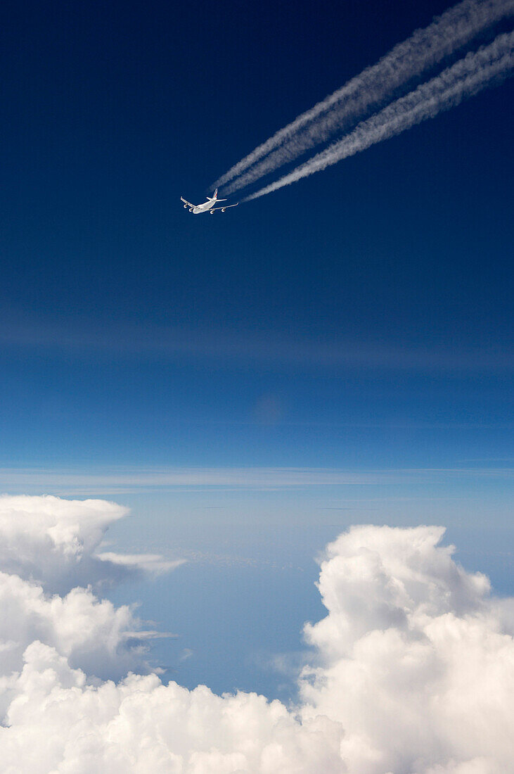Aircraft with contrails flying over the clouds in front of a dark blue sky