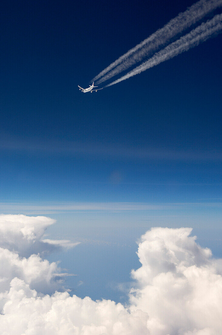 Flugzeug mit Kondensstreifen über den Wolken vor dunkelblauem Himmel