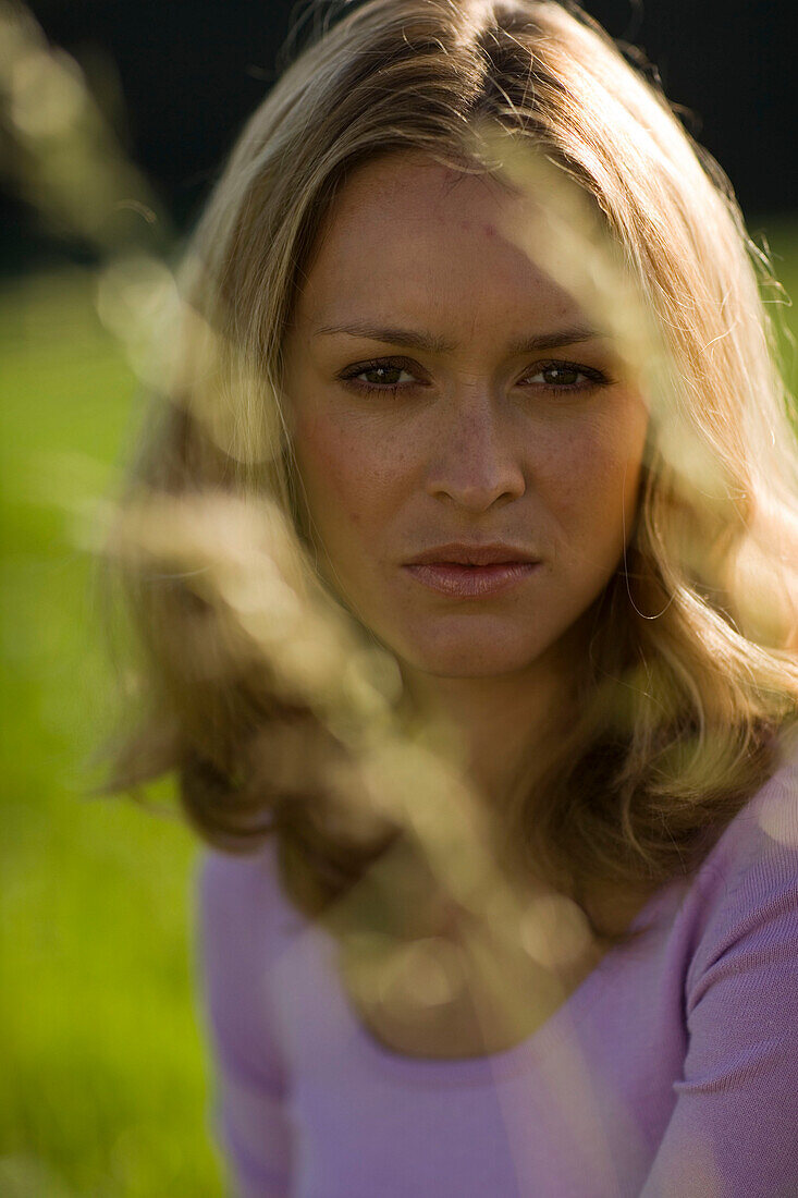 Young woman sitting on meadow, Blades of grass in foreground