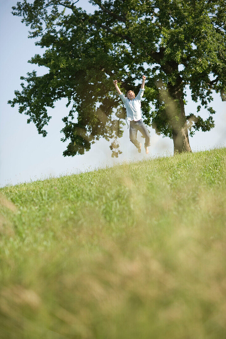 Young man jumping high on meadow, arm raised