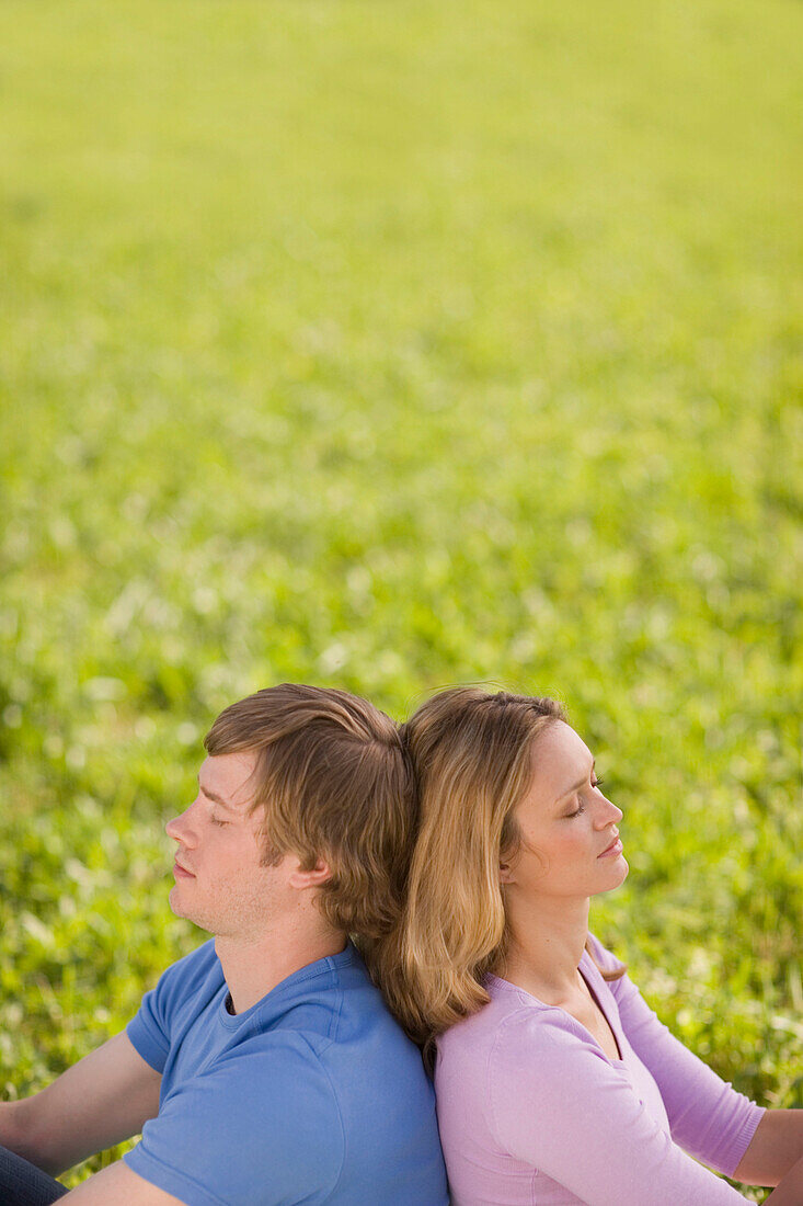 Couple sitting back to back on meadow