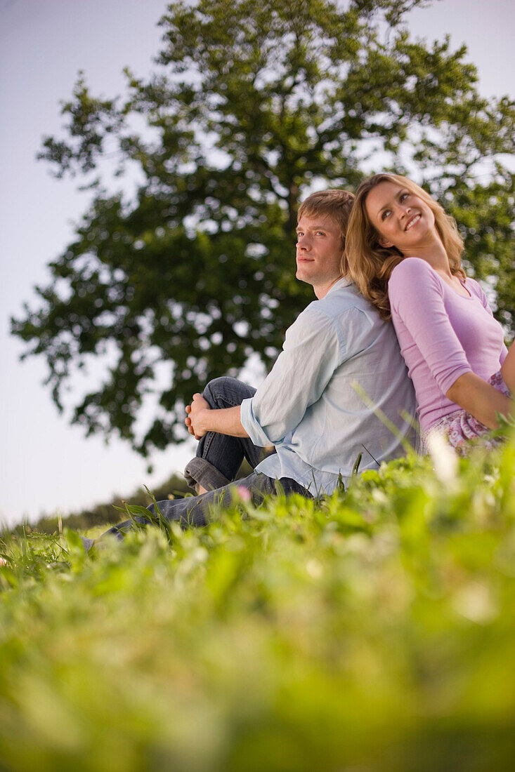 Couple sitting back to back on meadow