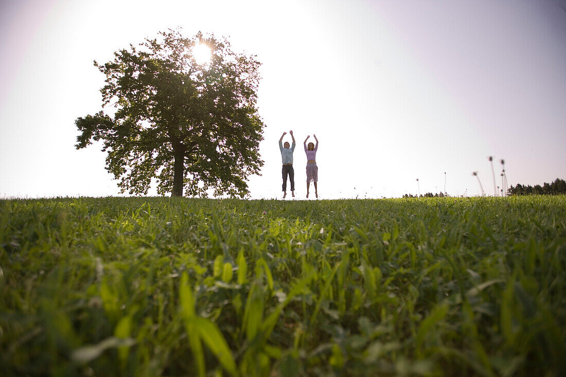 Couple jumping on meadow, raising arms