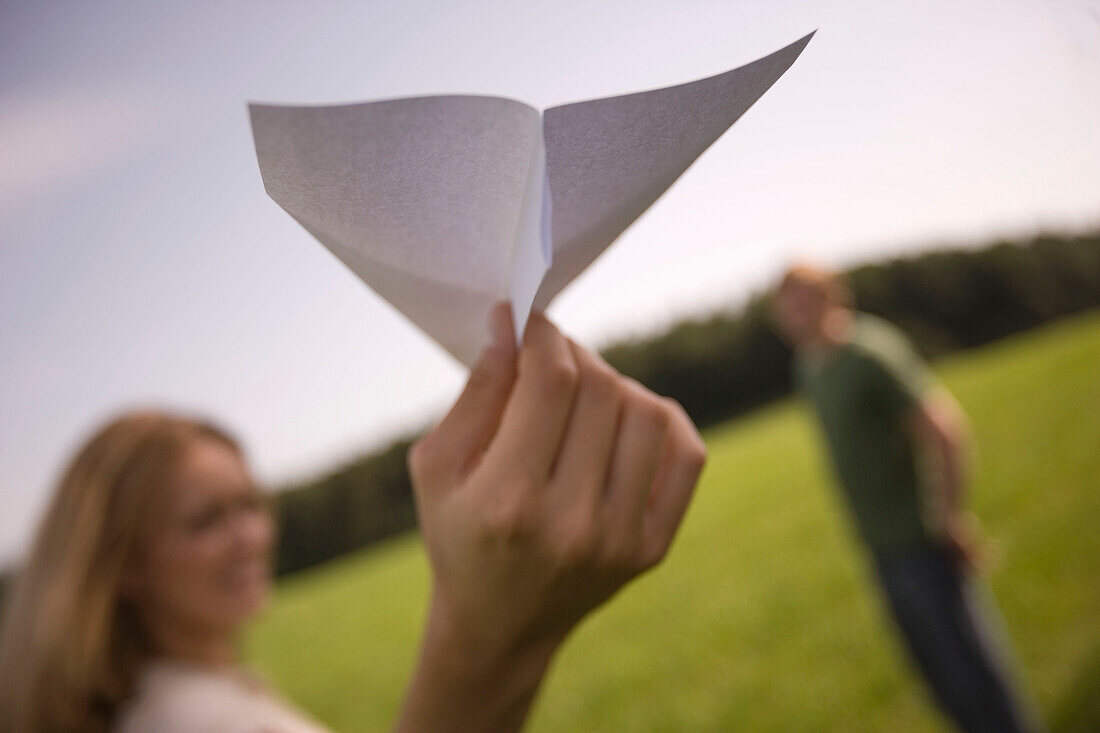 Junge Frau mit Papierflugzeug, auf einer Wiese