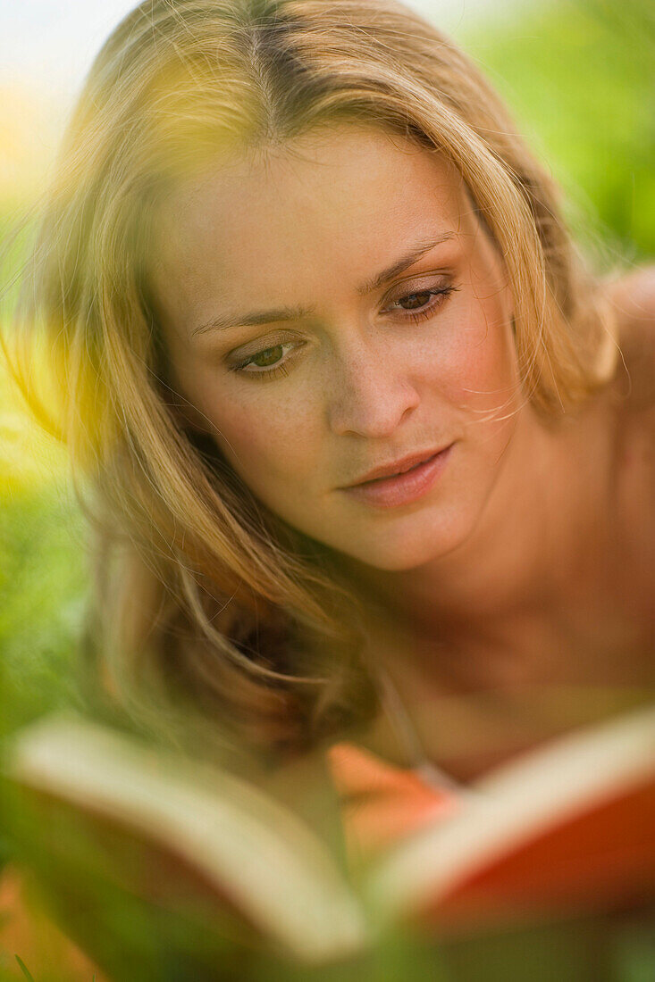 Young woman lying on meadow and reading book