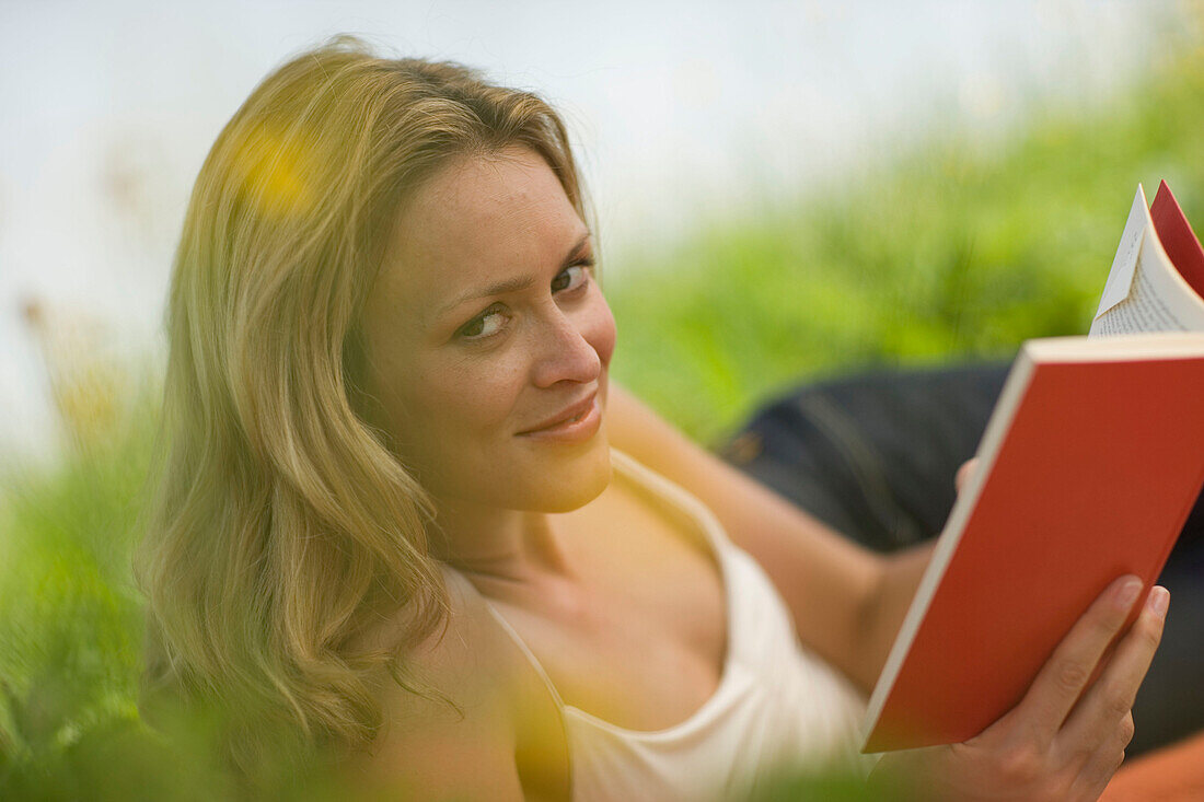 Junge Frau liegt in der Wiese und liest ein Buch