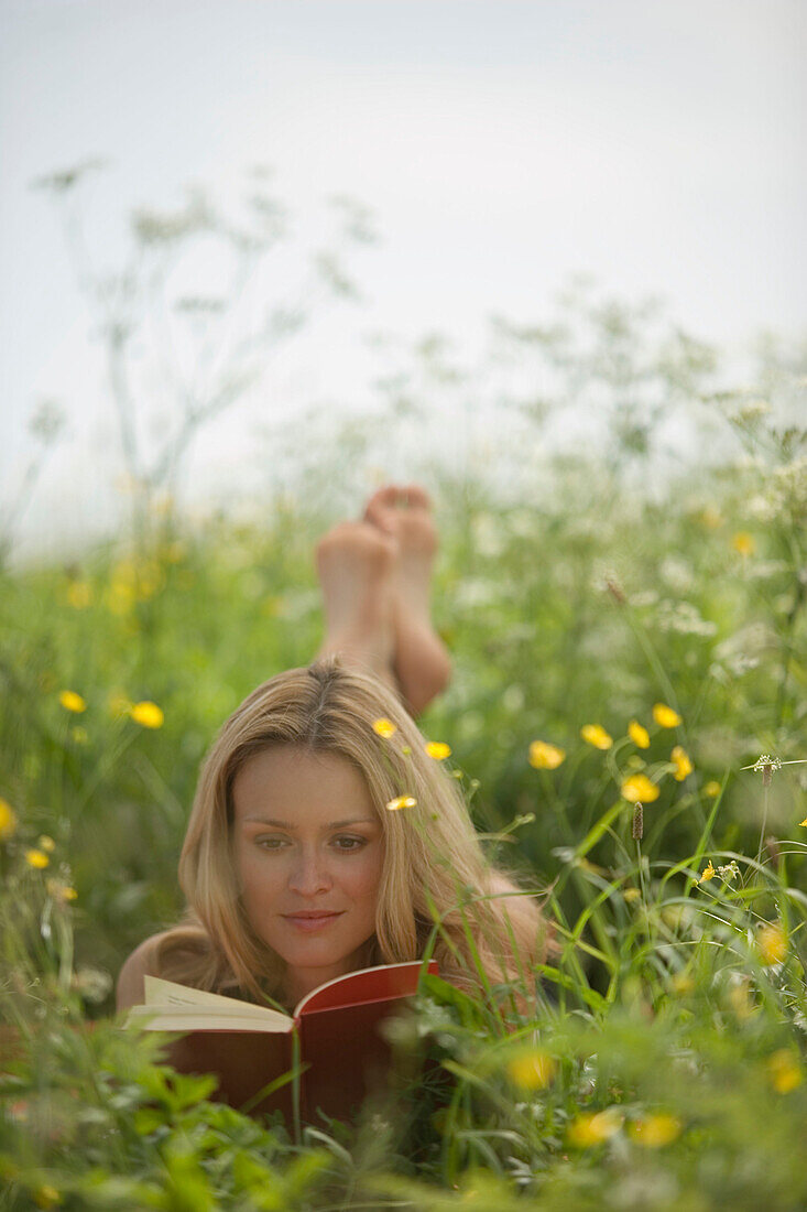 Junge Frau liegt in der Wiese und liest ein Buch