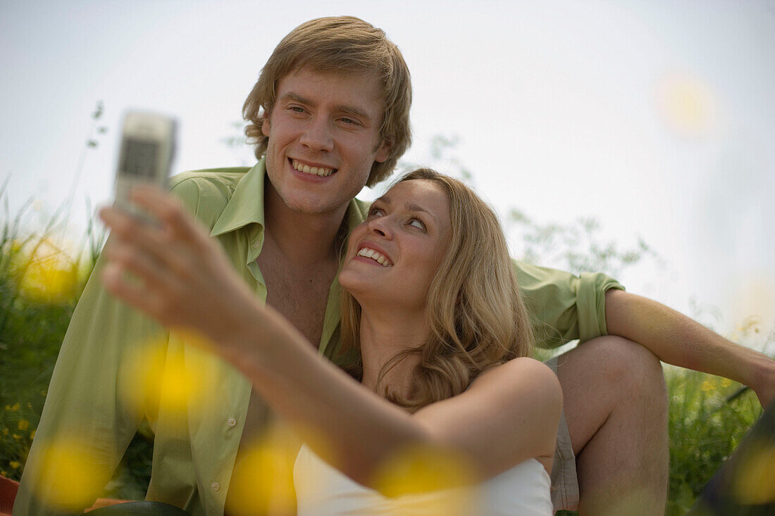 Young couple on meadow, woman taking picture with camera phone